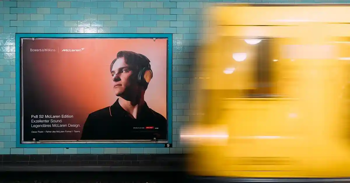Das Bild zeigt ein Bowers & Wilkins x McLaren Plakat am Bahnsteig einer Berliner U-Bahn-Station, davor fährt eine gelbe U-Bahn ein.