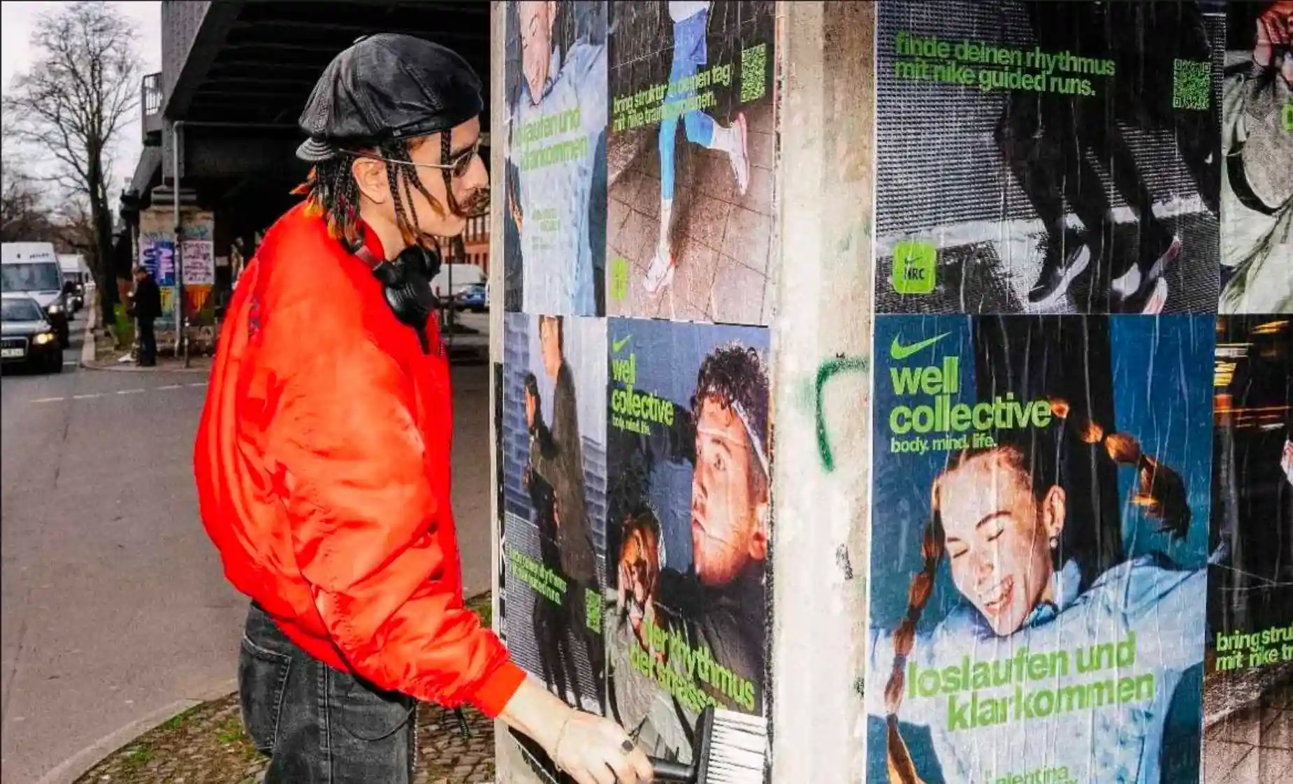 Das Bild zeigt einen Plakatierer von Echo Poster, der Nike Well Collective Plakate mit Kleisterbürste an eine Säule in Berlin klebt.